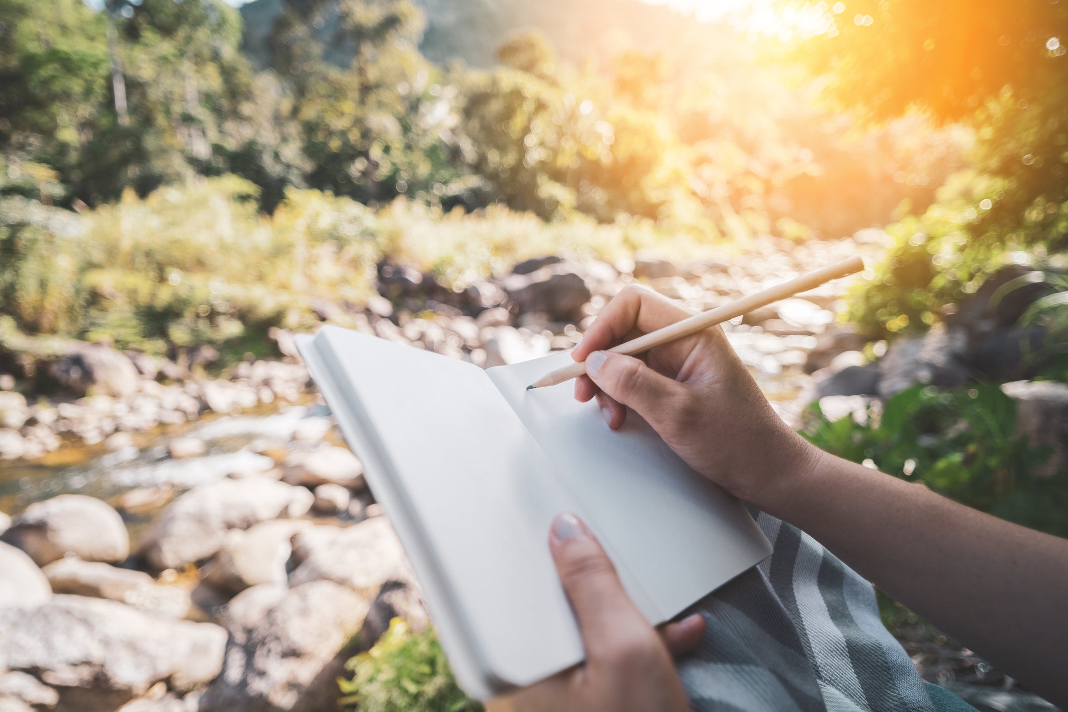 person writing in a notebook by a river