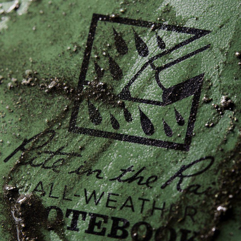 close up of olive green waterproof notebook with dirt on it 
