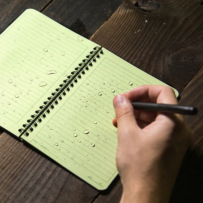 close up of person writing in a waterproof notebook on a wooden table
