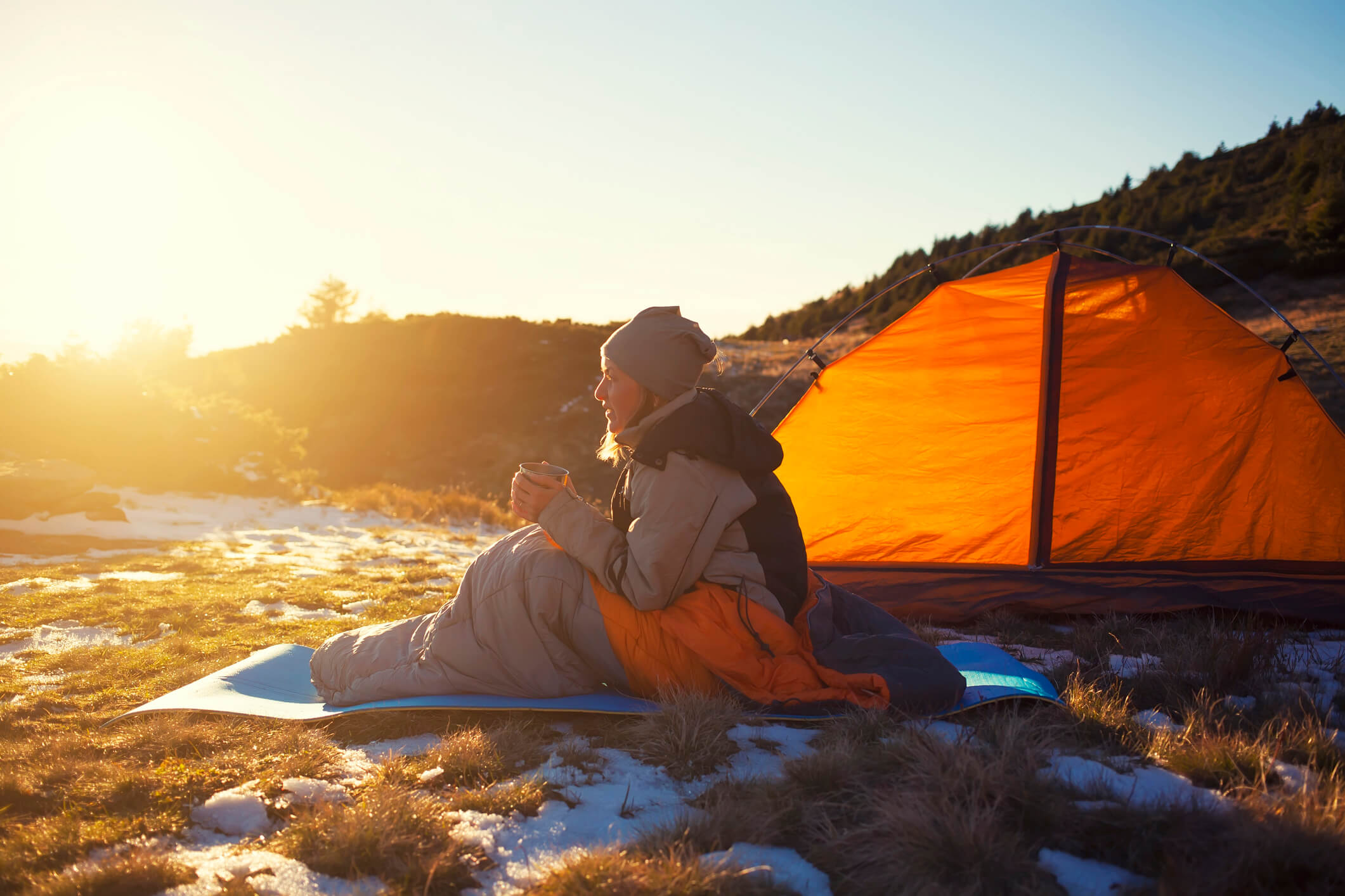 woman sat in front of a tent wearing winter clothes and holding a hot drink