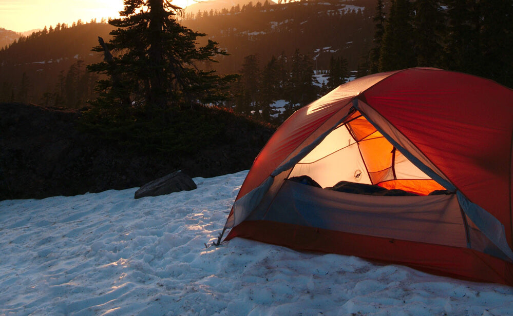 tent set up on snowy ground with hills and trees in the background